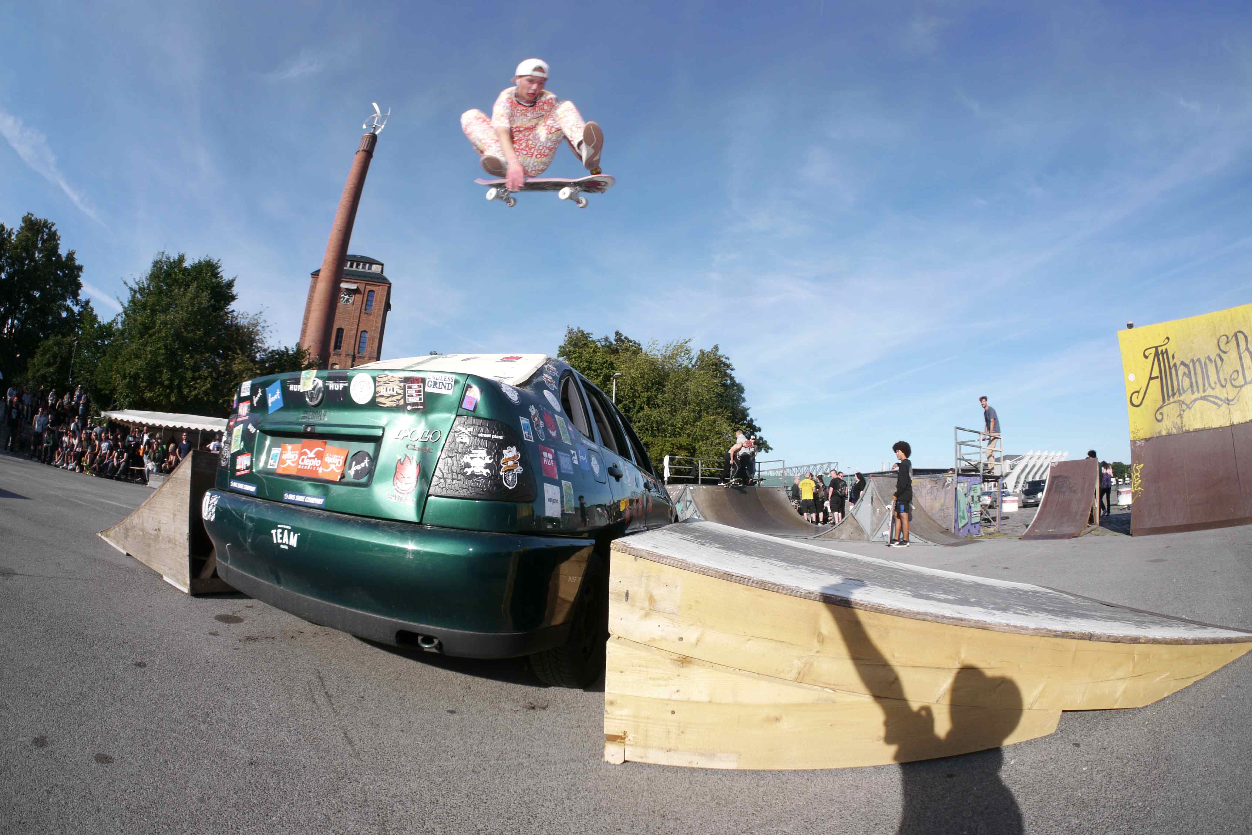 Ein Skater springt mit seinem Skateboard über ein altes Auto.