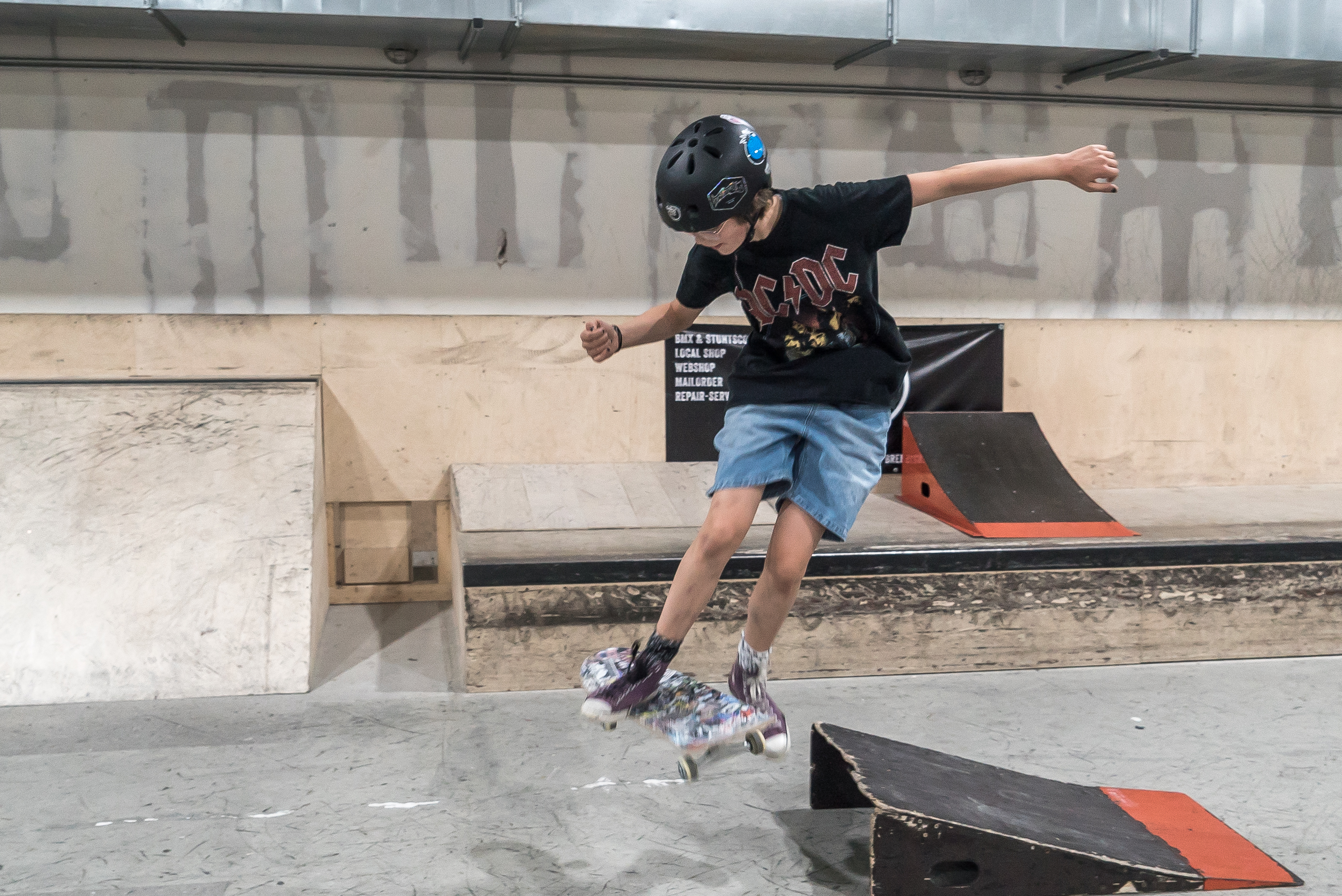 Ein Mädchen mit AC DC T-Shirt springt mit ihrem Skateboard über eine kleine Rampe.