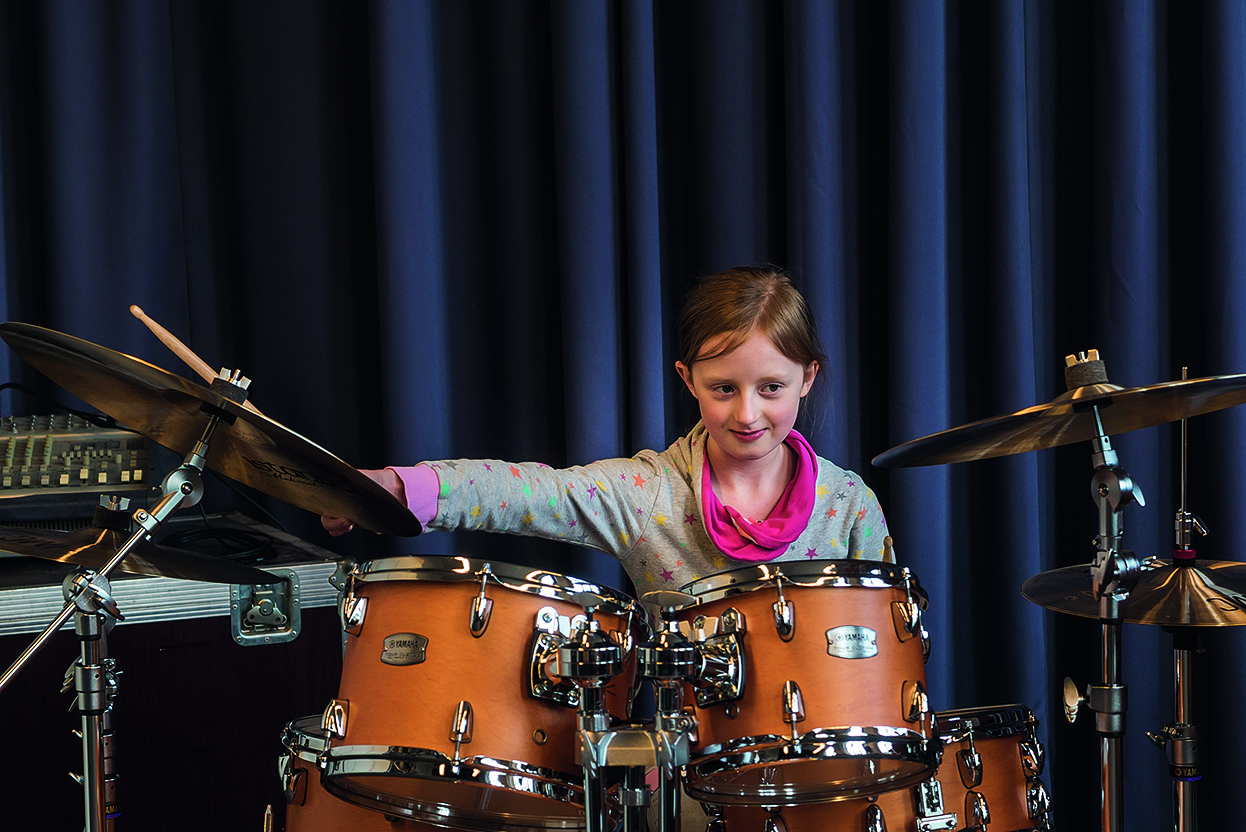 Eine junge Musikschülerin sitzt an einem Schlagzeug.